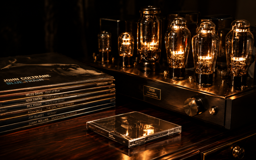 Stack of vinyl records and a CD on a wooden surface with glowing light bulbs in the background.